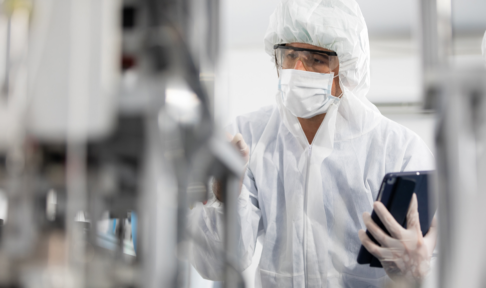 male engineers wearing personal protective equipment uniform(PPE) using tablet and checking medical face mask beside machine in laboratory