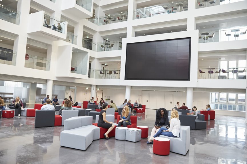 Students meeting in front of screen in atrium at university