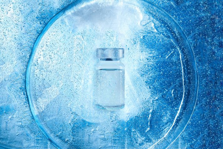 glass frozen ampoule with a virus vaccine on the texture of cold ice top view, background with backlight on the theme of pharmaceutical drugs from viral diseases.